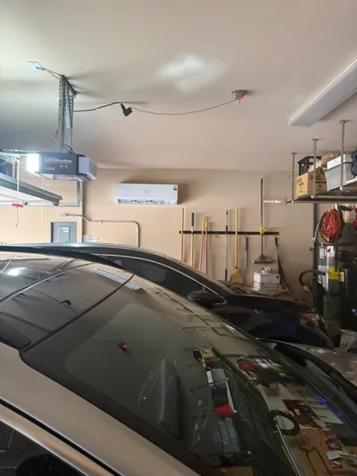 Ductless mini-split indoor unit installed above parked cars in a garage